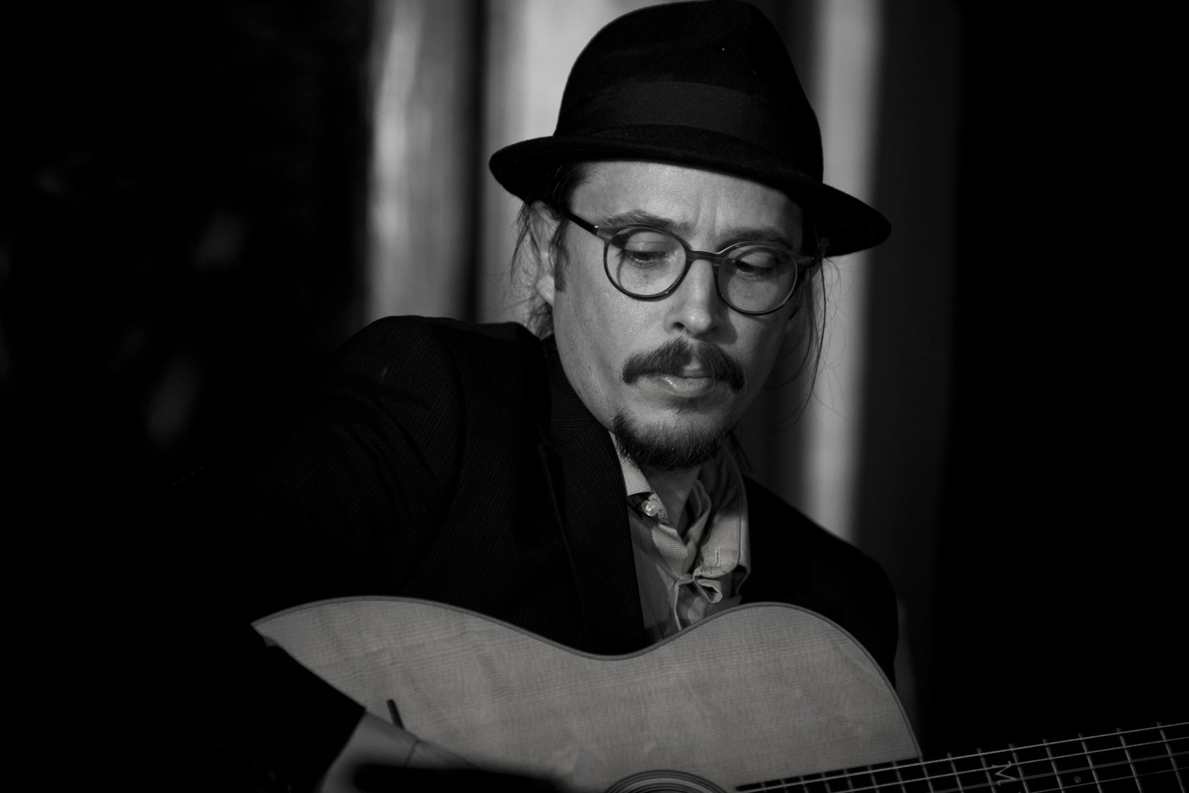 Black-and-white photo of Marc Wencelius with his guitar, wearing a hat and glasses
