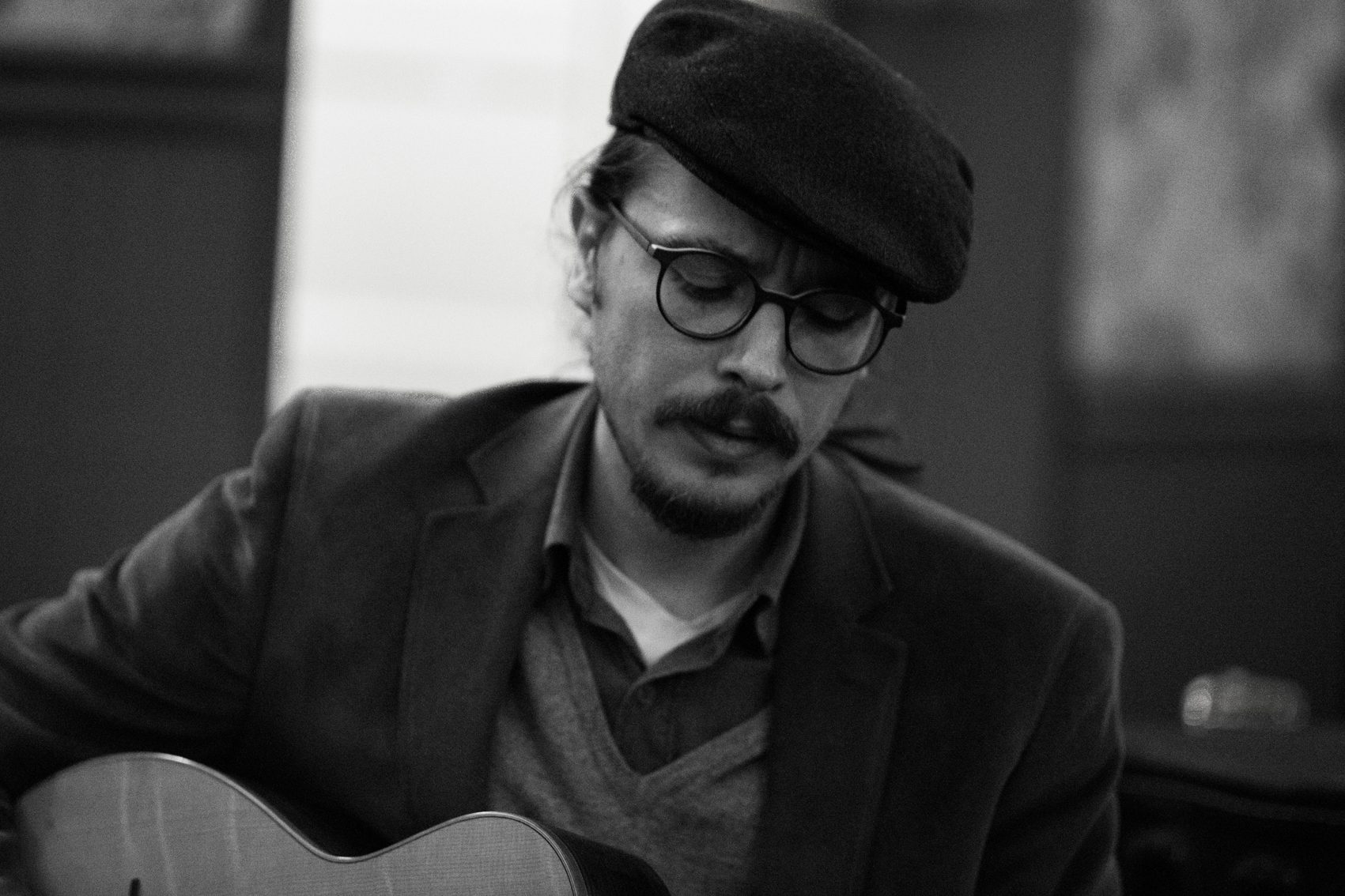 Black-and-white photo of Marc Wencelius in a flat cap playing guitar