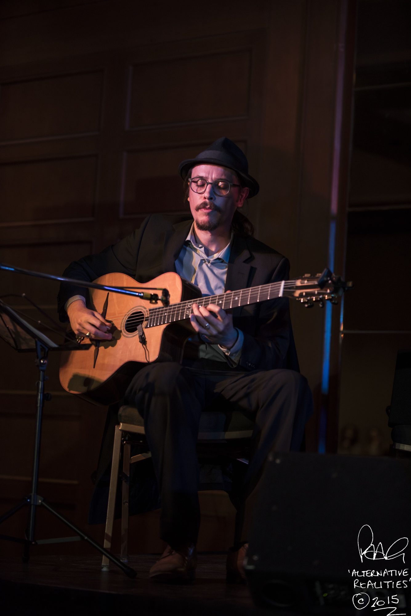 Marc Wencelius seated on stage with his guitar, 2015