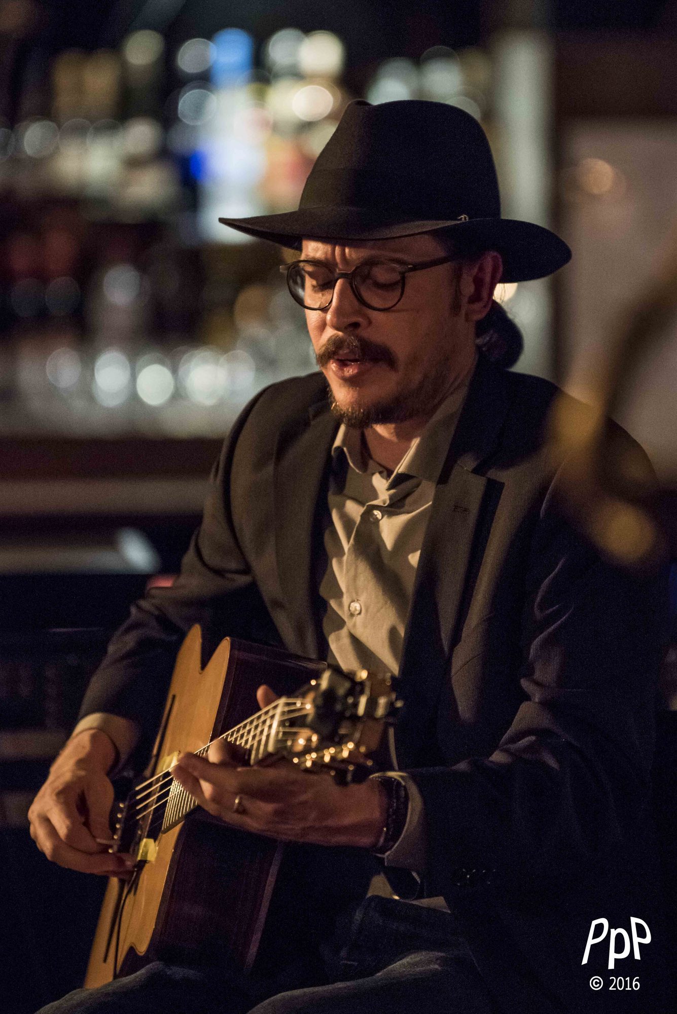 Marc Wencelius in a fedora playing guitar in a bar, 2016