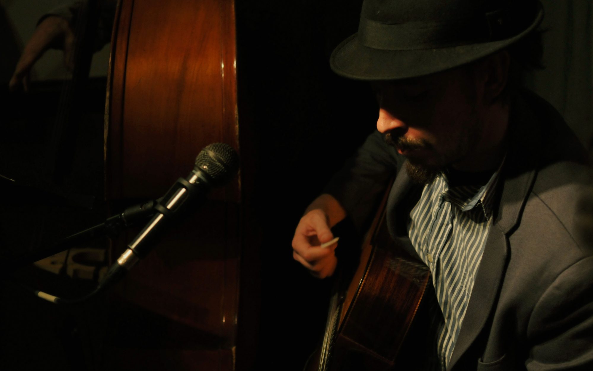 Marc Wencelius playing guitar in low light next to a double bass