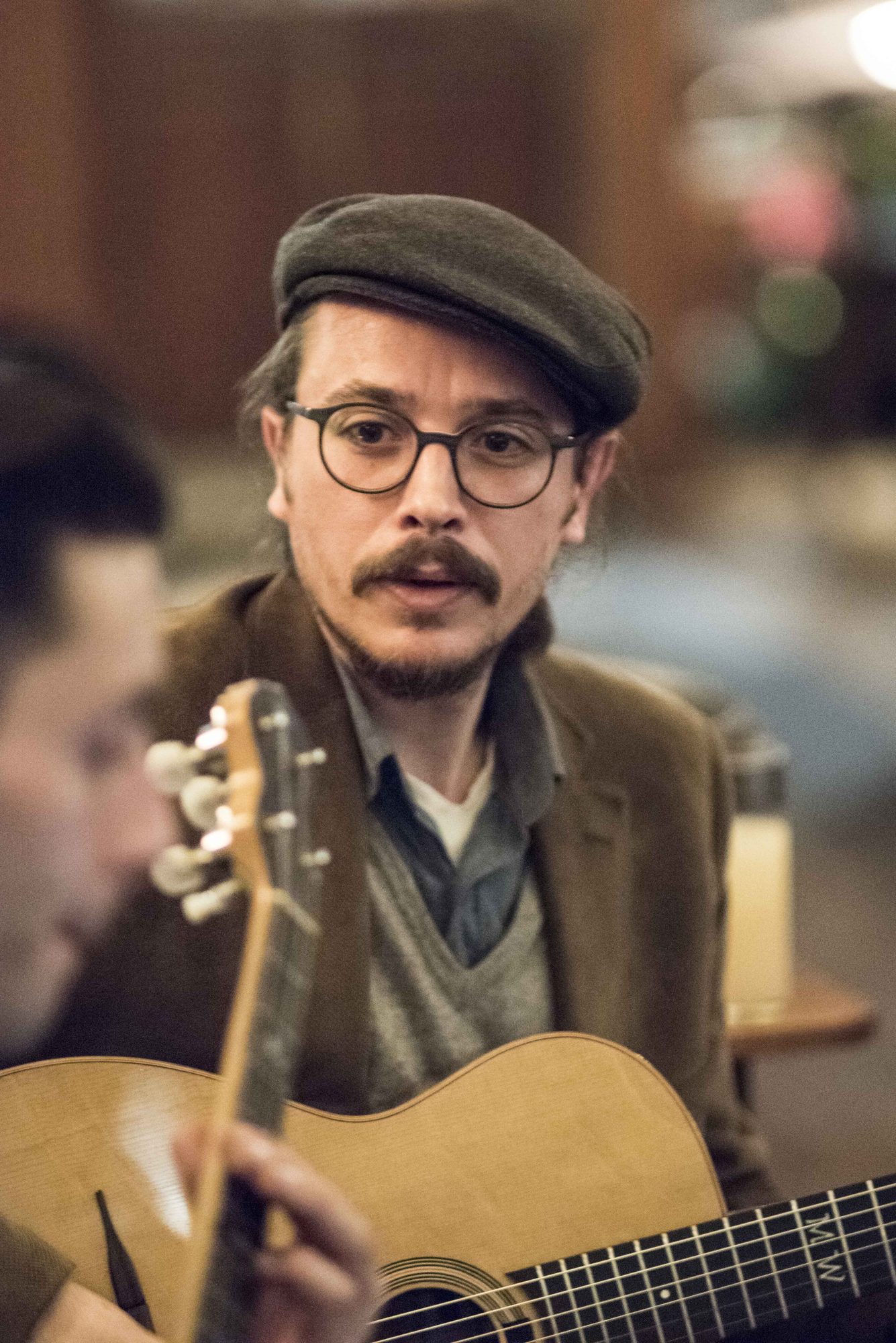 Portrait of Marc Wencelius in a flat cap with his acoustic guitar
