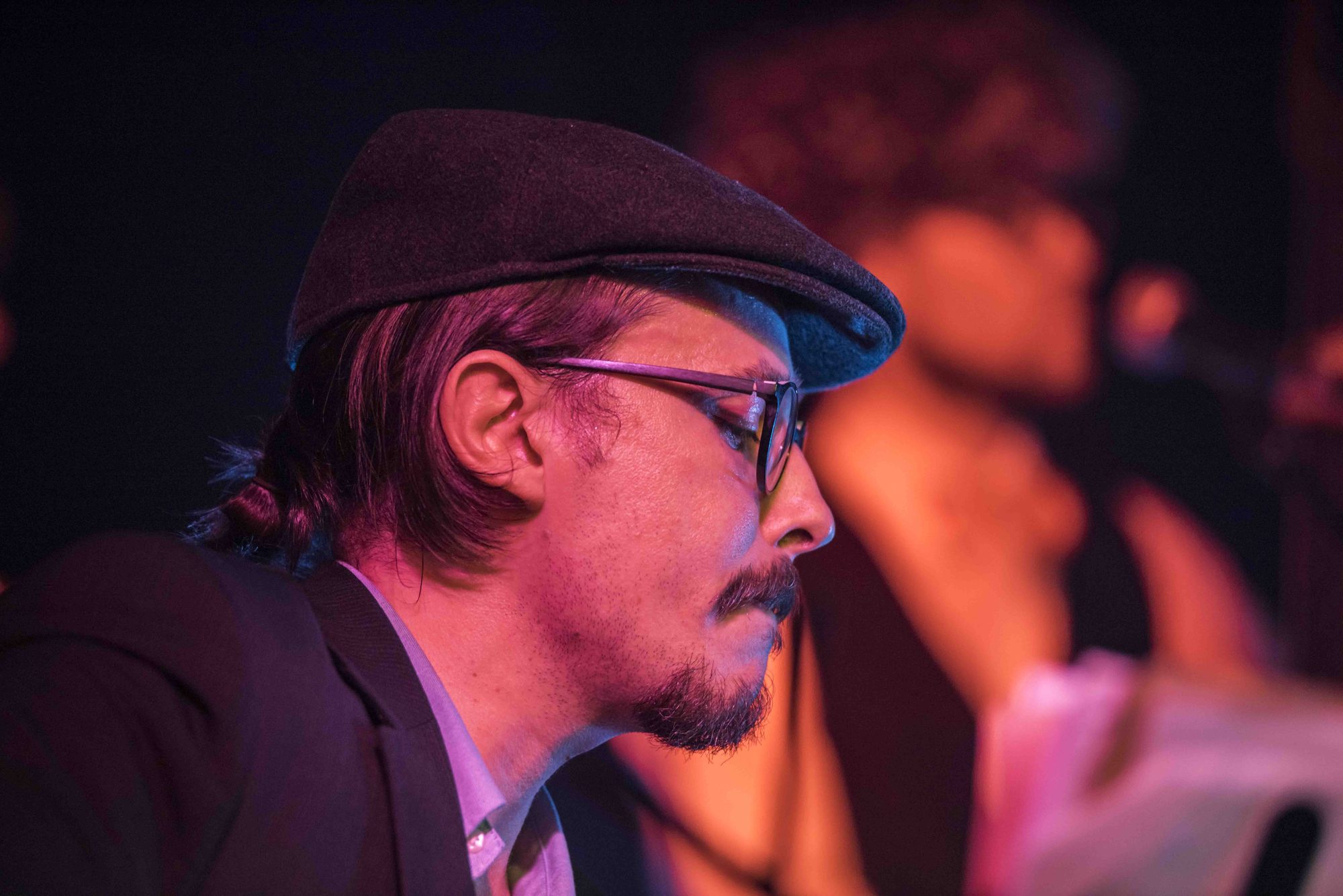 Close-up of Marc Wencelius in a flat cap and glasses under warm stage lights